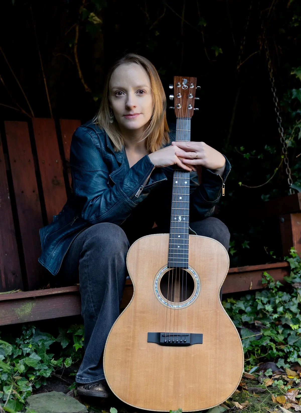 Amy Goddard holding an acoustic guitar in a warm natural light studio