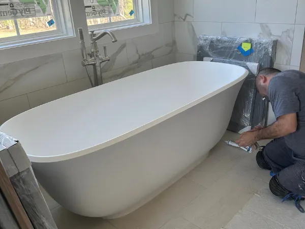 Plumber putting finishing touches on a freestanding bathtub in a luxury bathroom, representing high-end bathroom plumbing, home remodeling, fixture installation, plumbing craftsmanship, and premium residential plumbing services.