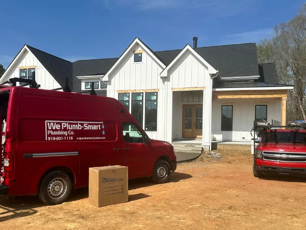 Plumb Smart Plumbing service van parked in front of a custom home under construction, representing custom home plumbing, new construction plumbing, builder partnerships, quality workmanship, and professional residential construction services.