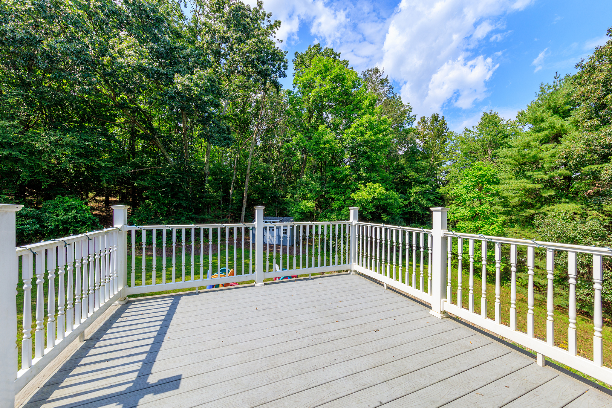Composite deck with white railing overlooking a wooded backyard