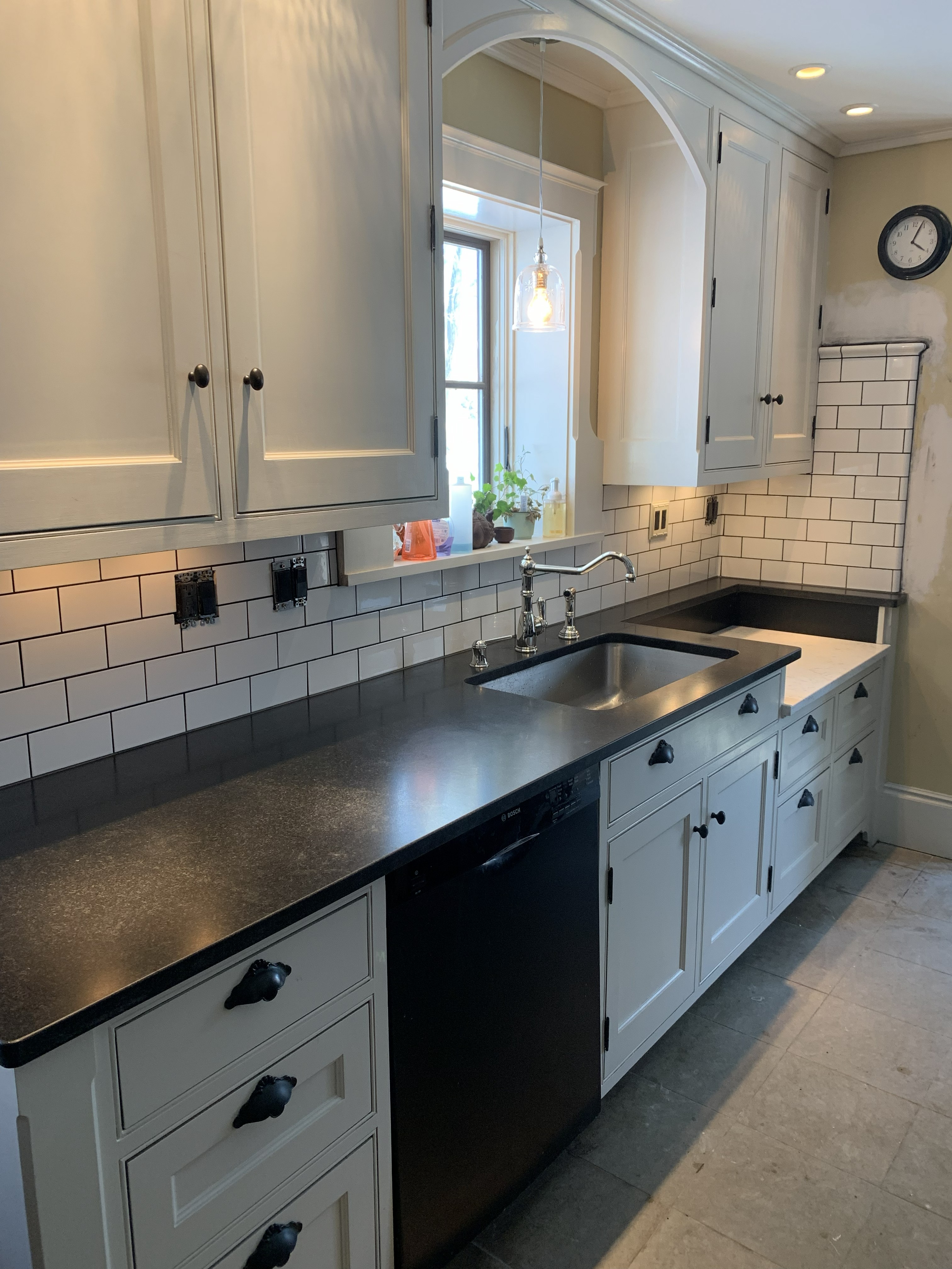 Kitchen remodel with black countertops, white cabinets, and sink under window