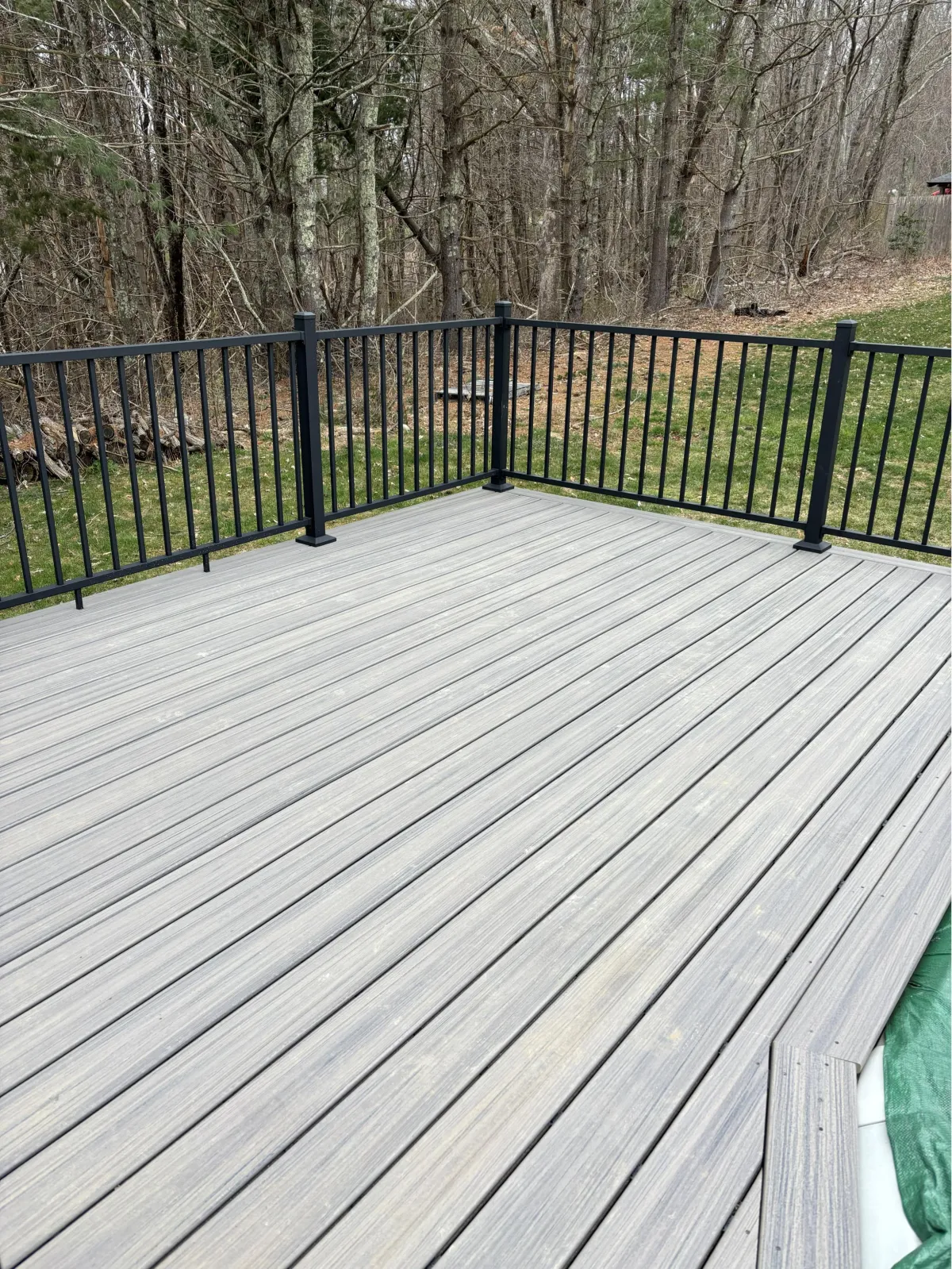 Composite deck surface with black metal railing overlooking backyard
