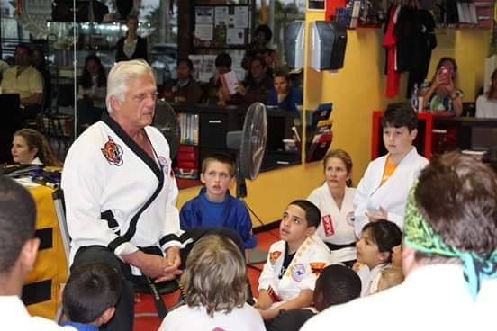 A dynamic group of diverse adults practicing Hapkido in a sunlit modern living room, each performing a different technique with focused expressions.