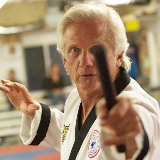 A dynamic group of diverse adults practicing Hapkido in a sunlit modern living room, each performing a different technique with focused expressions.