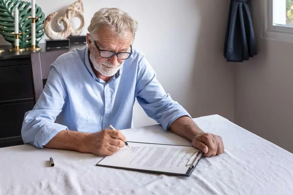 An older man signing a legal document at a table during probate administration.