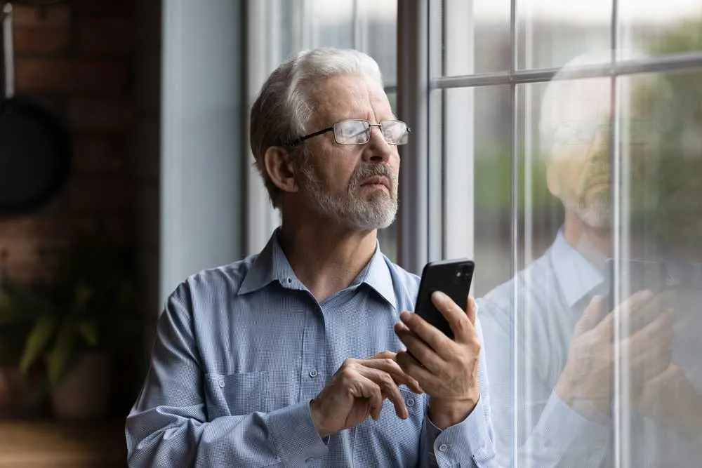 An older man looking at his phone through a window while engaged in probate administration.