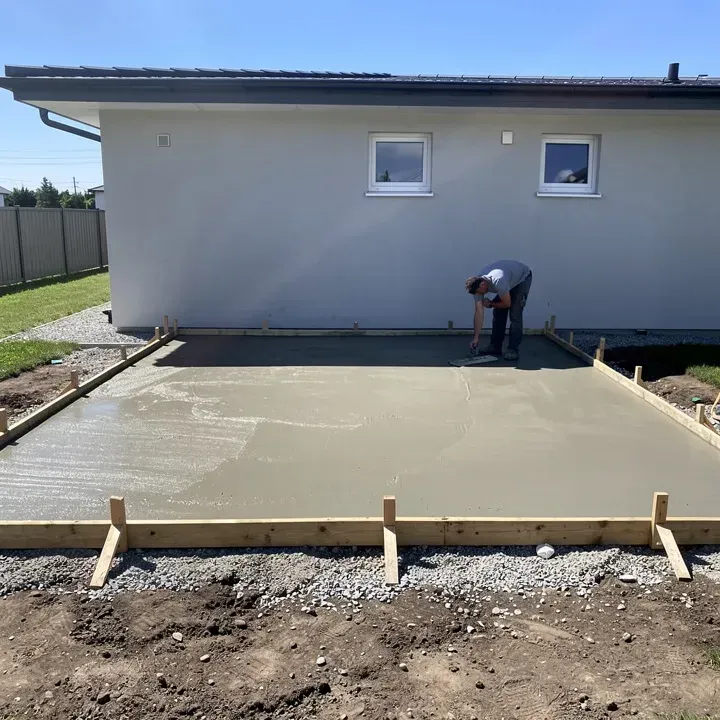 Concrete contractor seen from behind smoothing freshly poured concrete on a residential patio slab attached to the rear of a house in Warrensville Heights, Ohio.