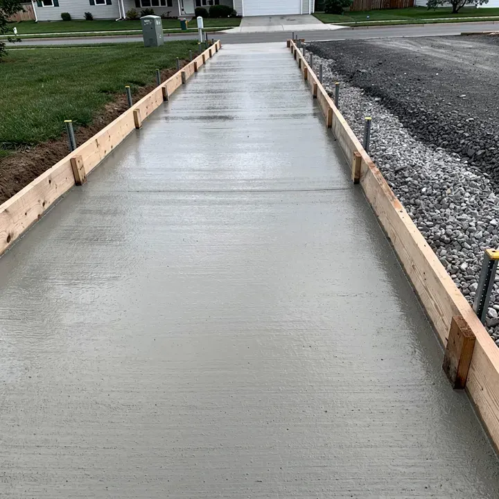 Freshly poured concrete sidewalk section with form boards in place along a residential front yard.