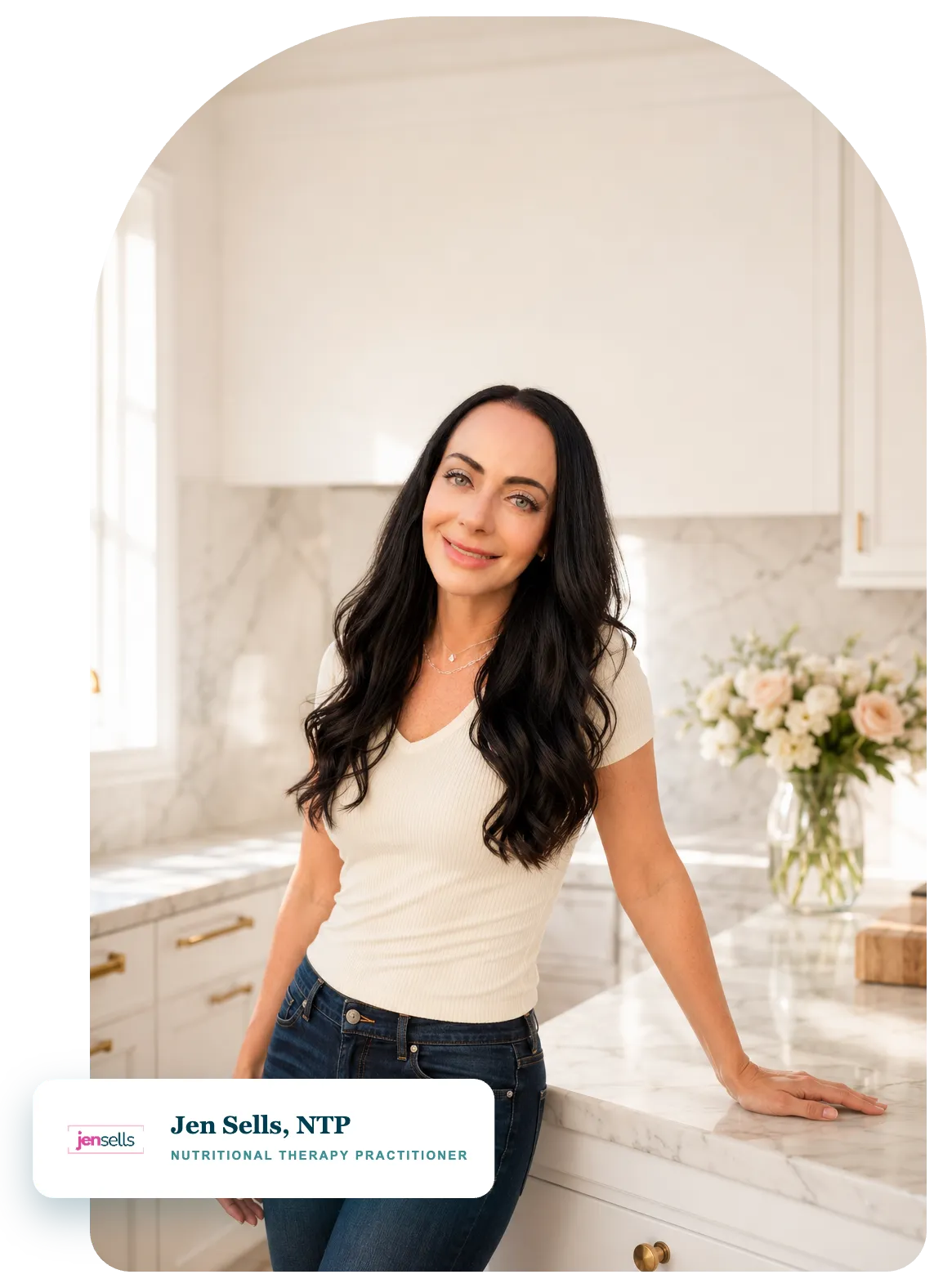 Jen Sells, Nutritional Therapy Practitioner, smiling in her bright white kitchen with marble counters and fresh flowers