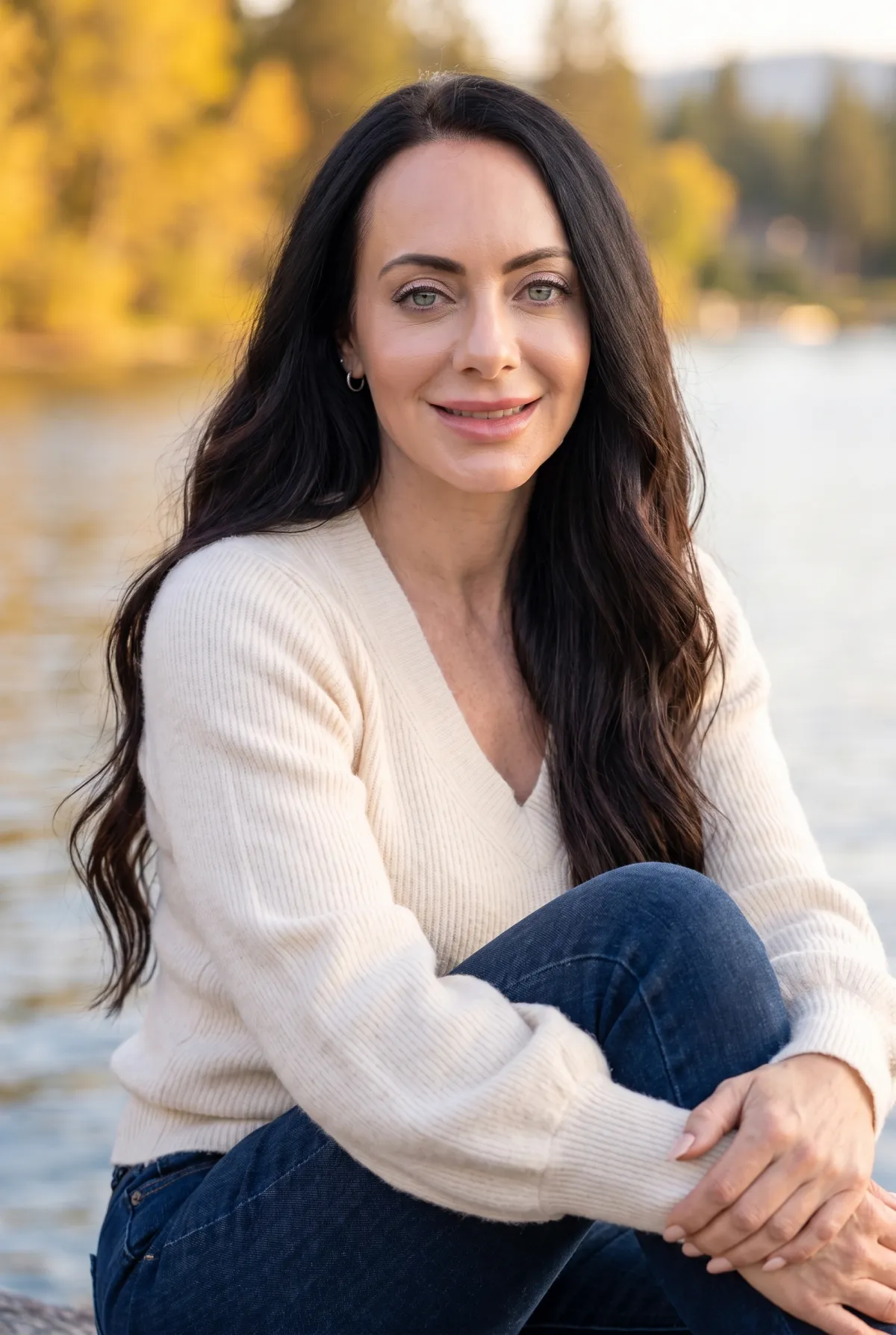 Portrait of Jen Sells outdoors at golden hour by a lake with autumn foliage