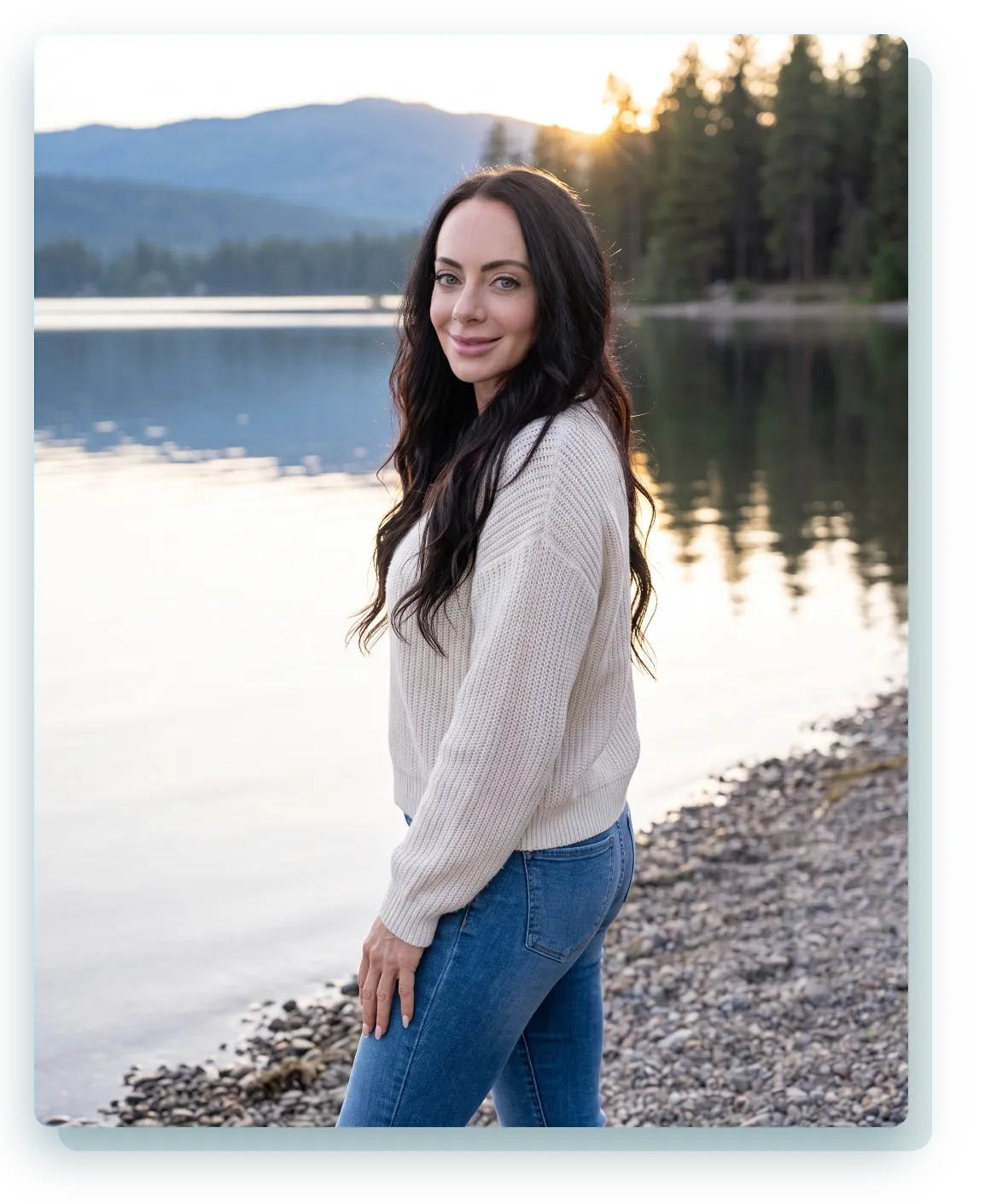 Jen standing by a lake at golden hour with pine forest and mountains in Idaho