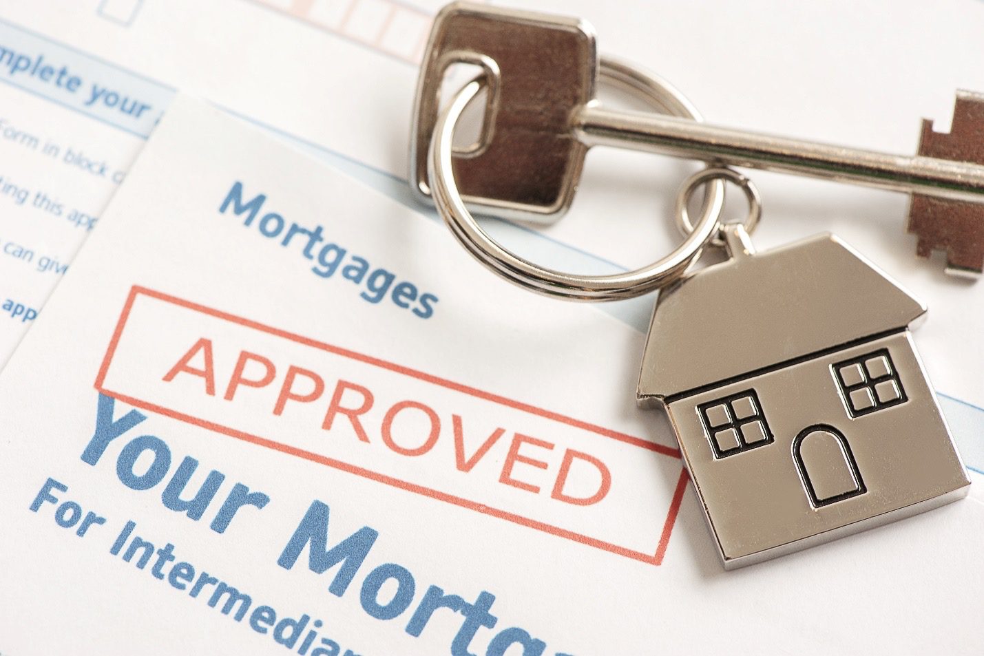 Close up of mortgage approved document with a shiny house key and keychain resting on top