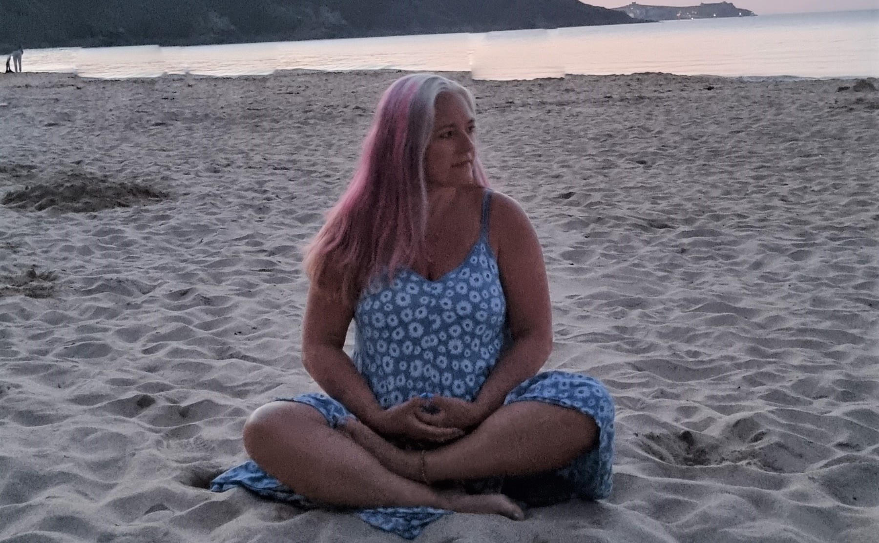 Julie sitting on the sand with the sun setting on the background.