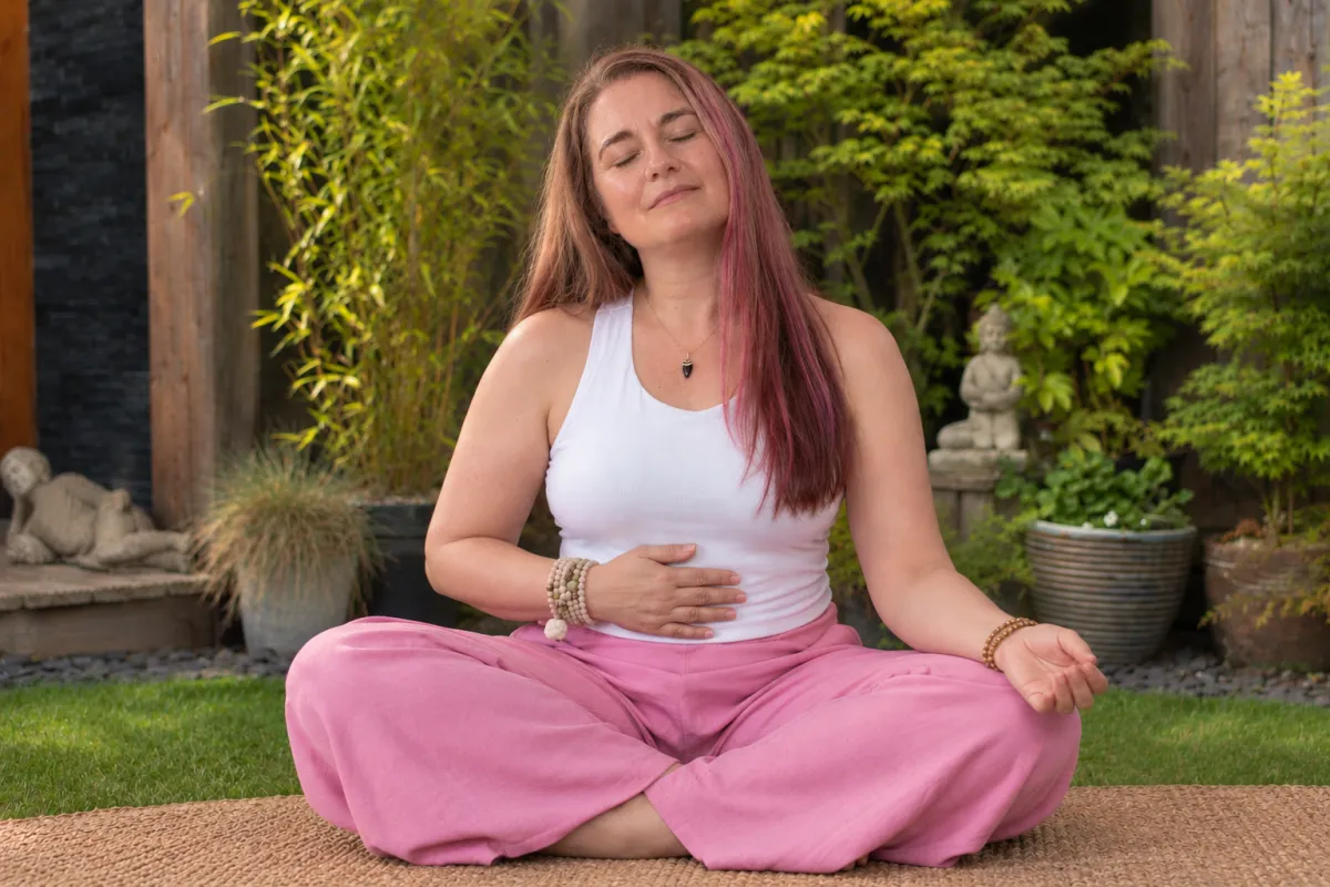 Julie in a grounded seated posture, hand at the belly or solar plexus — calm, embodied, not overtly staged.