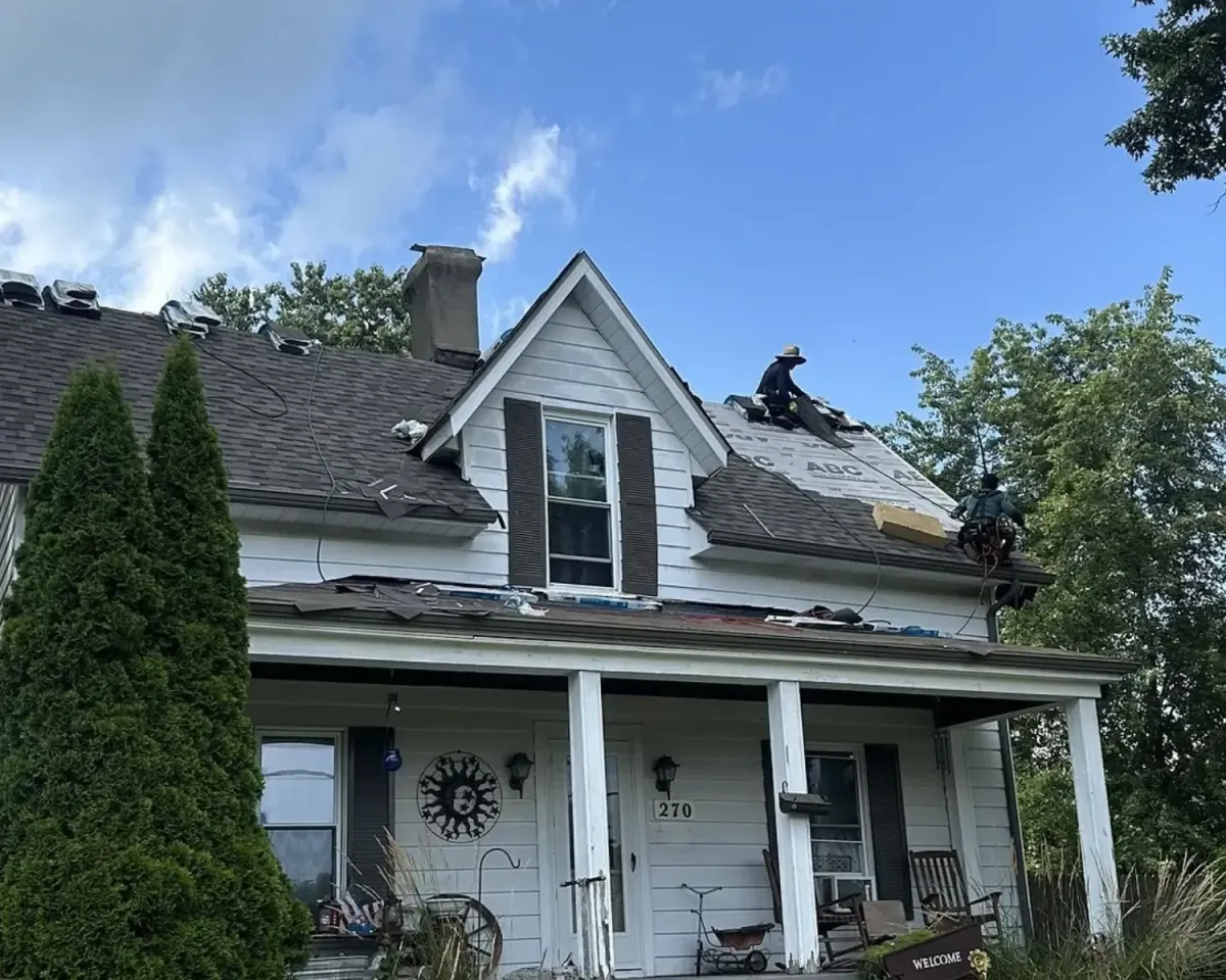 Roofing crew installing new asphalt shingles on a residential home, with underlayment exposed and workers using safety equipment on the roof.