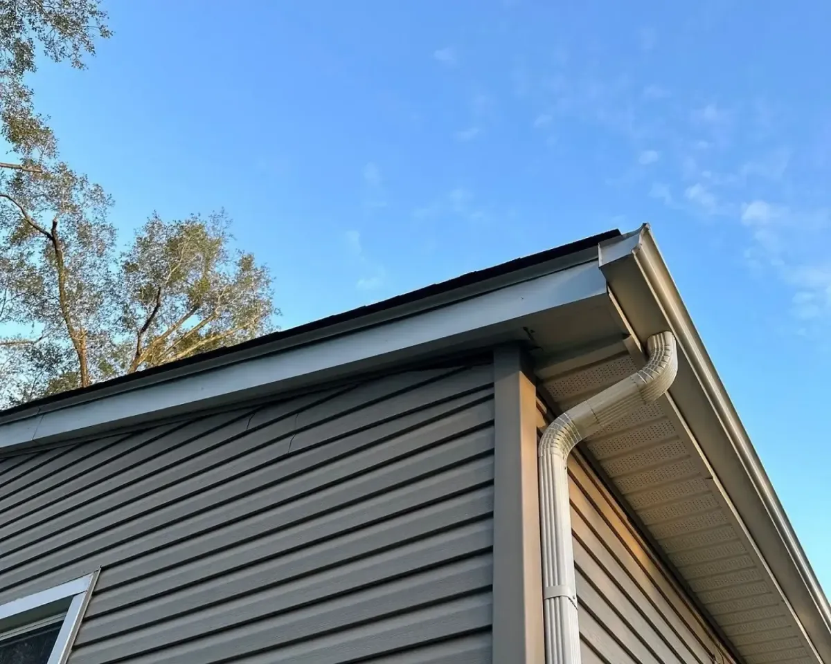 Close-up of newly installed aluminum gutters and downspout on a residential home with vinyl siding and vented soffit.
