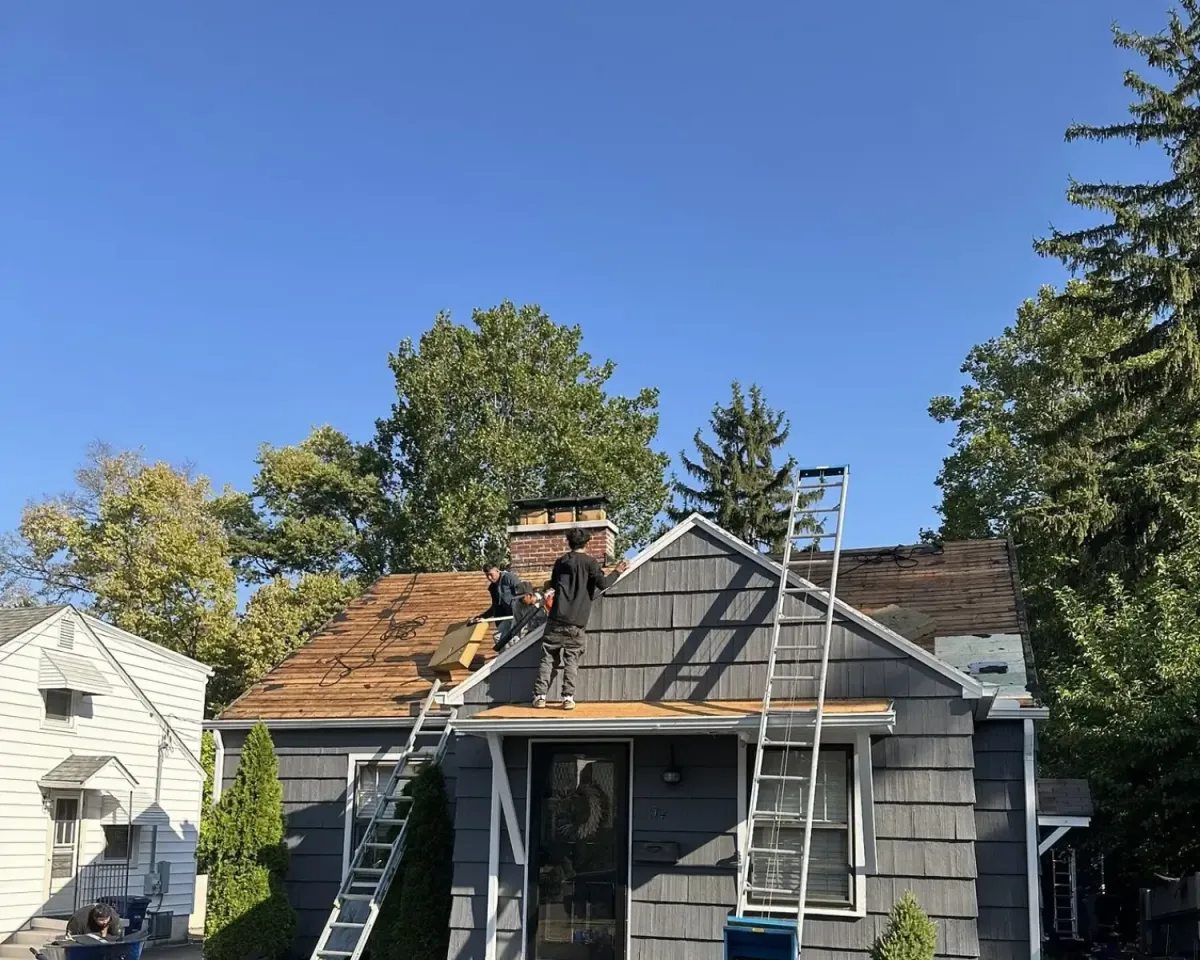 Roofers performing residential roof repair, removing old shingles and installing new roofing materials using ladders and safety equipment.
