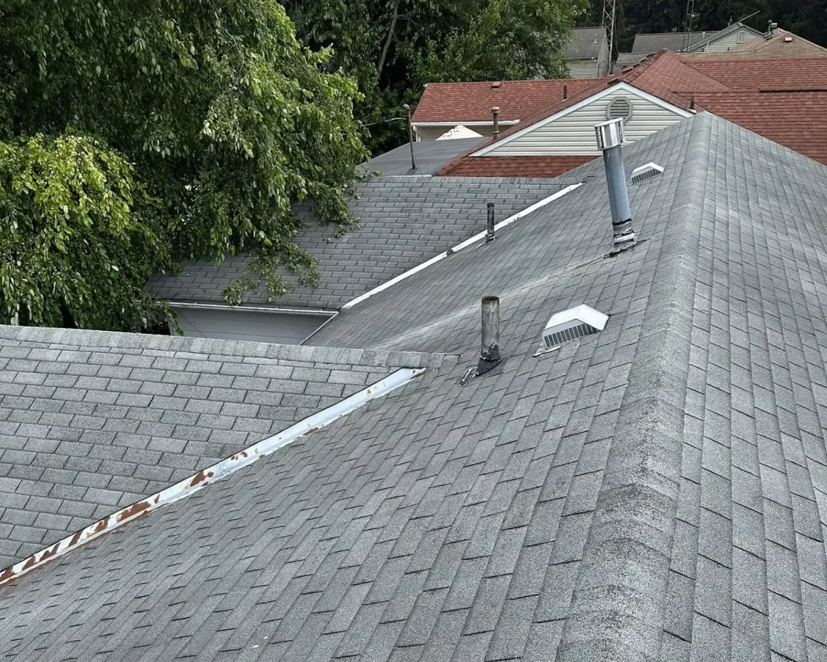 Aerial view of a residential roof showing asphalt shingles, roof vents, flashing, and ridge lines during a roof inspection.