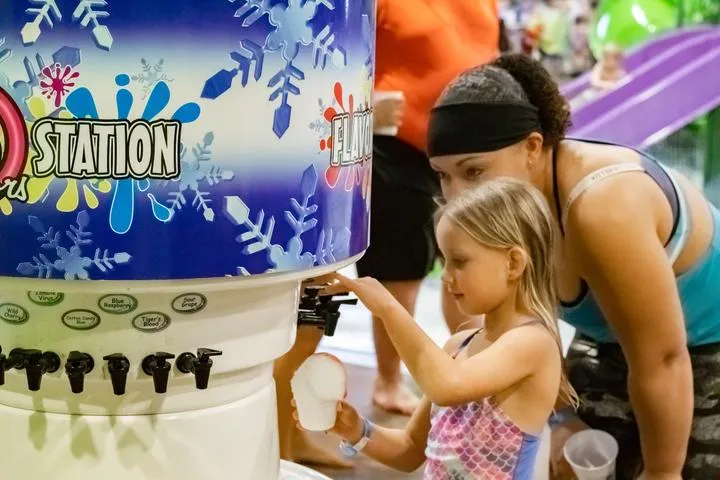A girl making herself a snow cone from the Flavor Station in Chaos Water Park