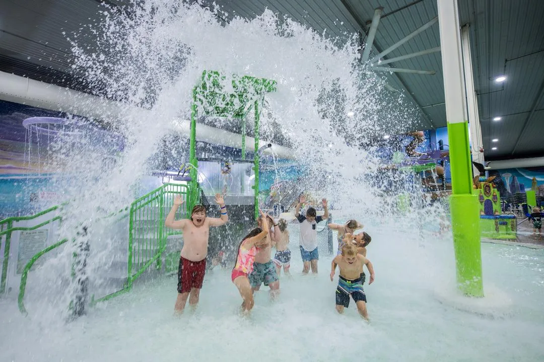 Kids standing under the dump bucket at the indoor aquatic playground in Chaos Water Park