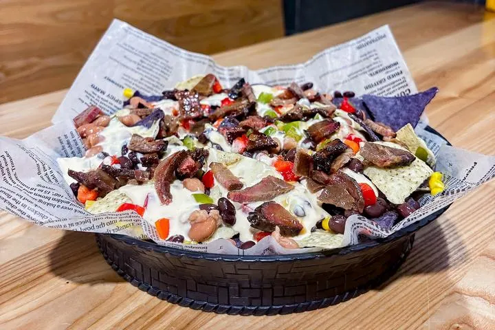 City Eats Cowboy Nachos with black beans, pinto beans, corn, peppers, tomatoes, cilantro, queso, and beef brisket over tortilla chips.