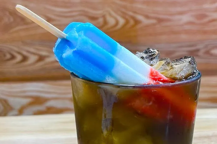 City Eats Rocket Pop cocktail with Twisted Tea, Blue Curacao, and grenadine topped with a Bomb Pop.