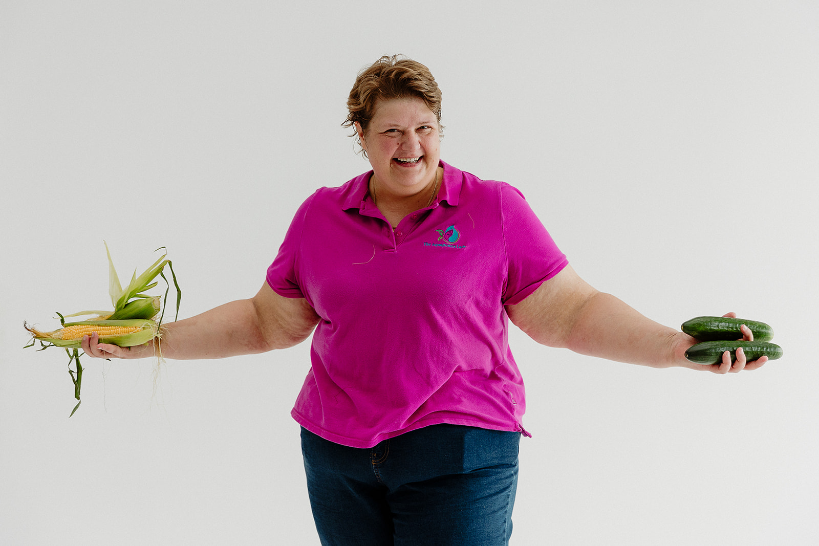 Candy holding freshly harvested corn and cucumbers while smiling.
