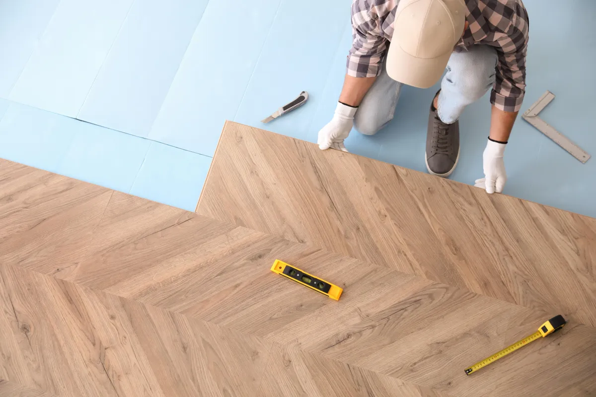 Installer laying herringbone wood-look flooring with measuring tools during installation.