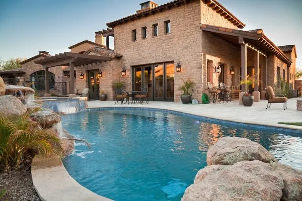 Stone home with a pool and patio at sunset