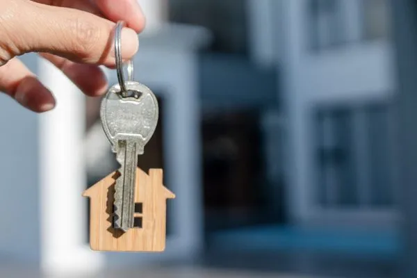 Hand holding a house key with a wooden house keychain
