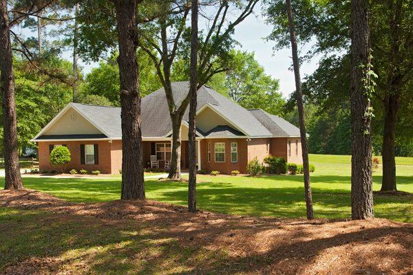 Brick home with a large green yard surrounded by trees