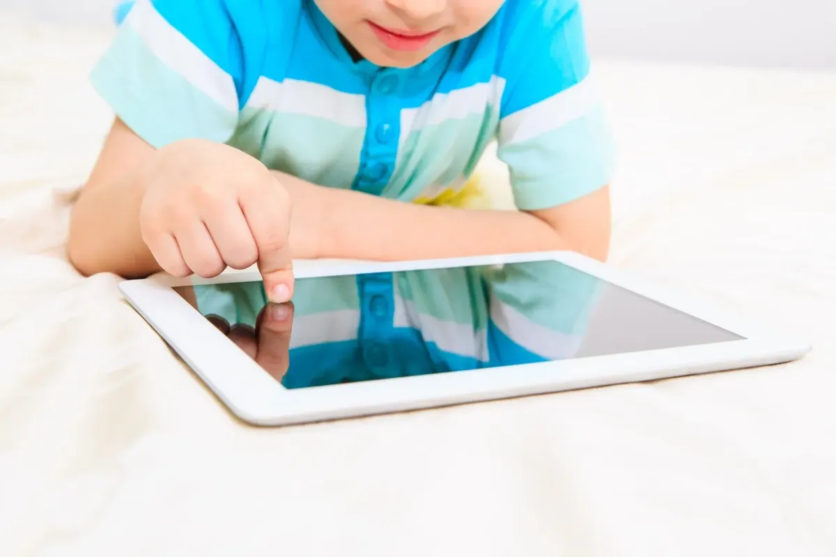 Child with headset smiles as he engages with laptop
