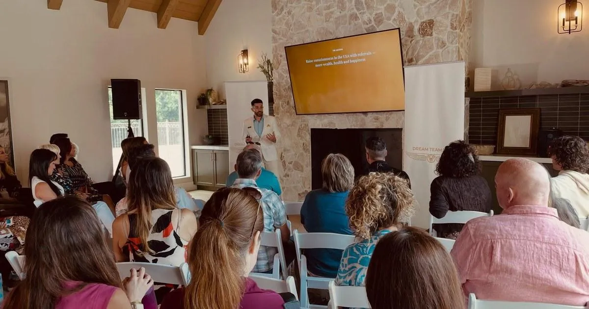 Business coach presenting client acquisition and wealth-building strategies to an audience at a live event.