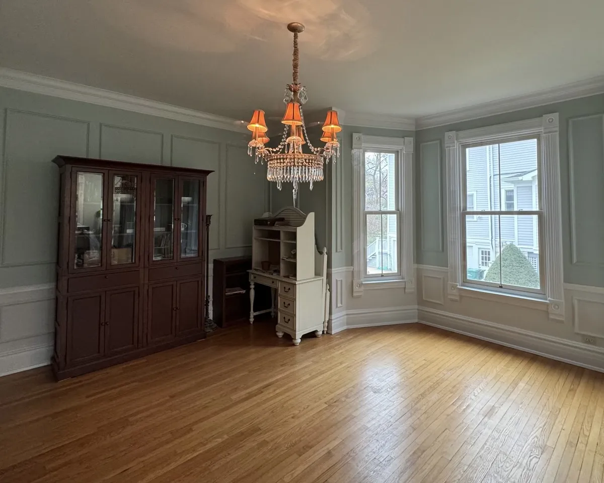 Residential dining room with light green painted walls, white trim, hardwood floors, and large windows, highlighting interior painting and detailed finishing.