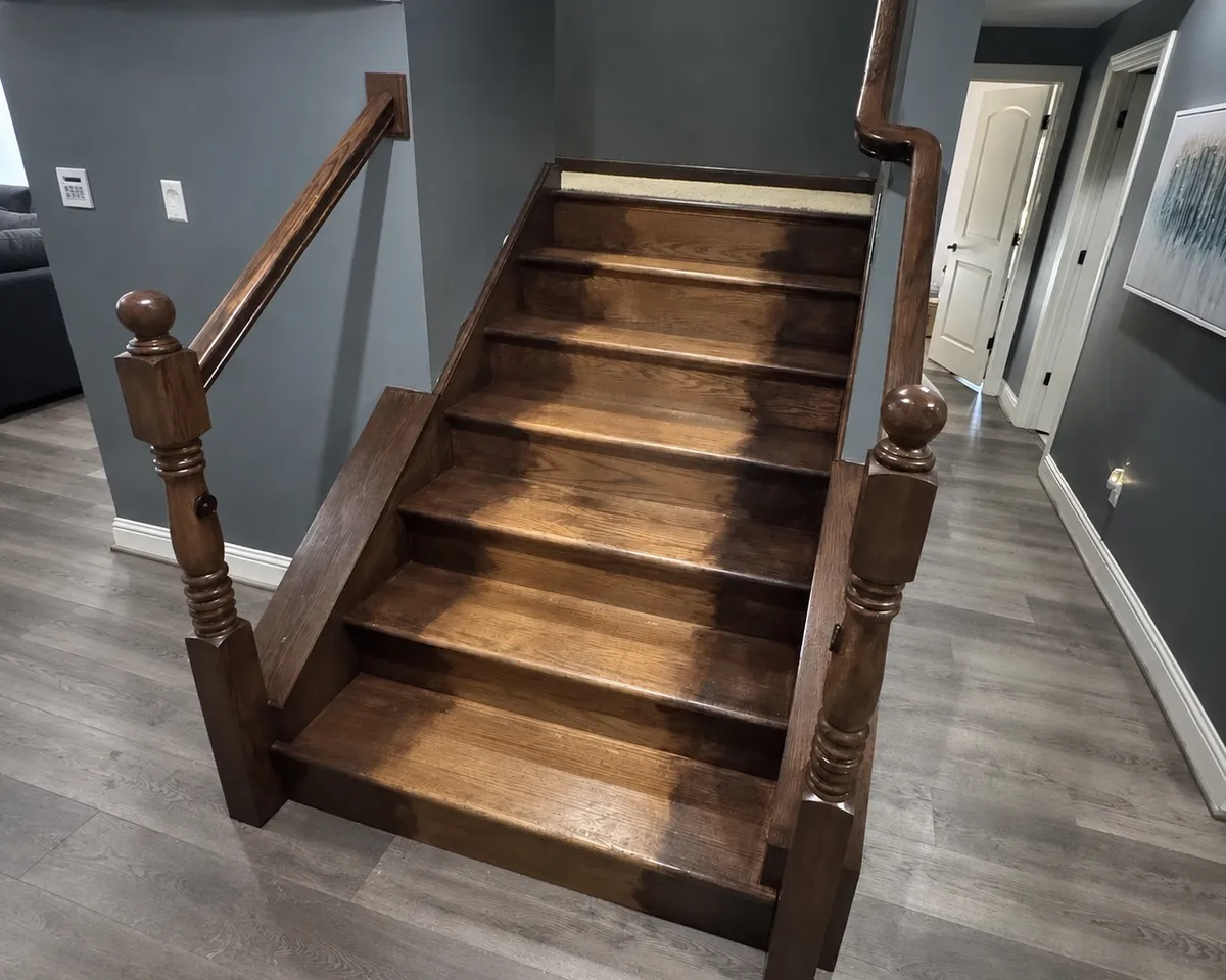 Wood staircase with dark stained treads, handrails, and wooden newel posts in a residential interior, showcasing wood refinishing and staining work.