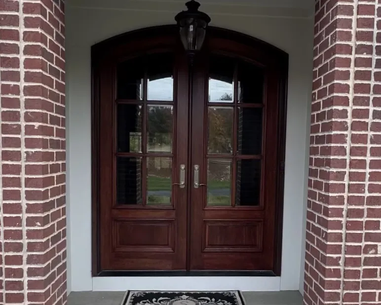 Dark stained wooden double entry doors with glass panels and decorative brick surround, showcasing exterior door and architectural woodwork finishing.