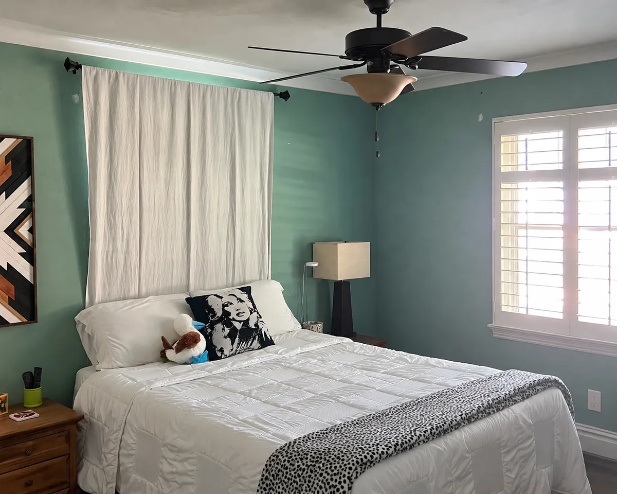 Bedroom with blue-green painted walls, white window trim, ceiling fan, and neutral furnishings, showcasing residential interior painting.