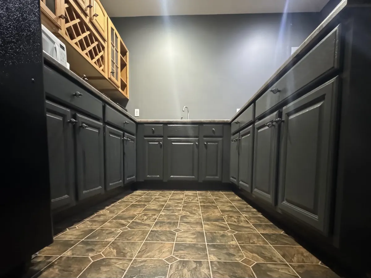Dark charcoal painted kitchen cabinets with raised panel doors, black hardware, and tile flooring, showcasing professional cabinet refinishing and painting.