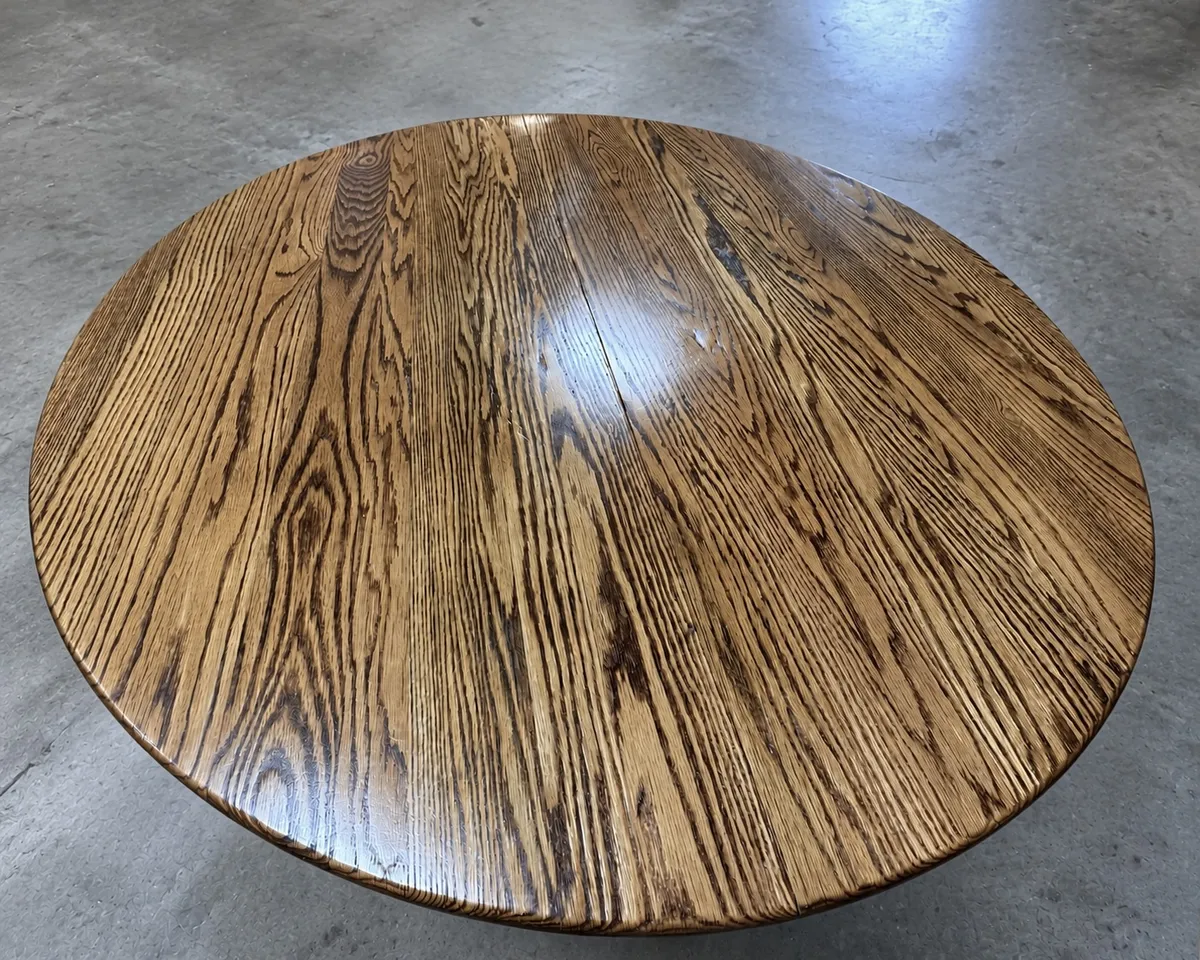 Round oak tabletop refinished with warm golden brown stain and a glossy protective finish that highlights the natural wood grain.