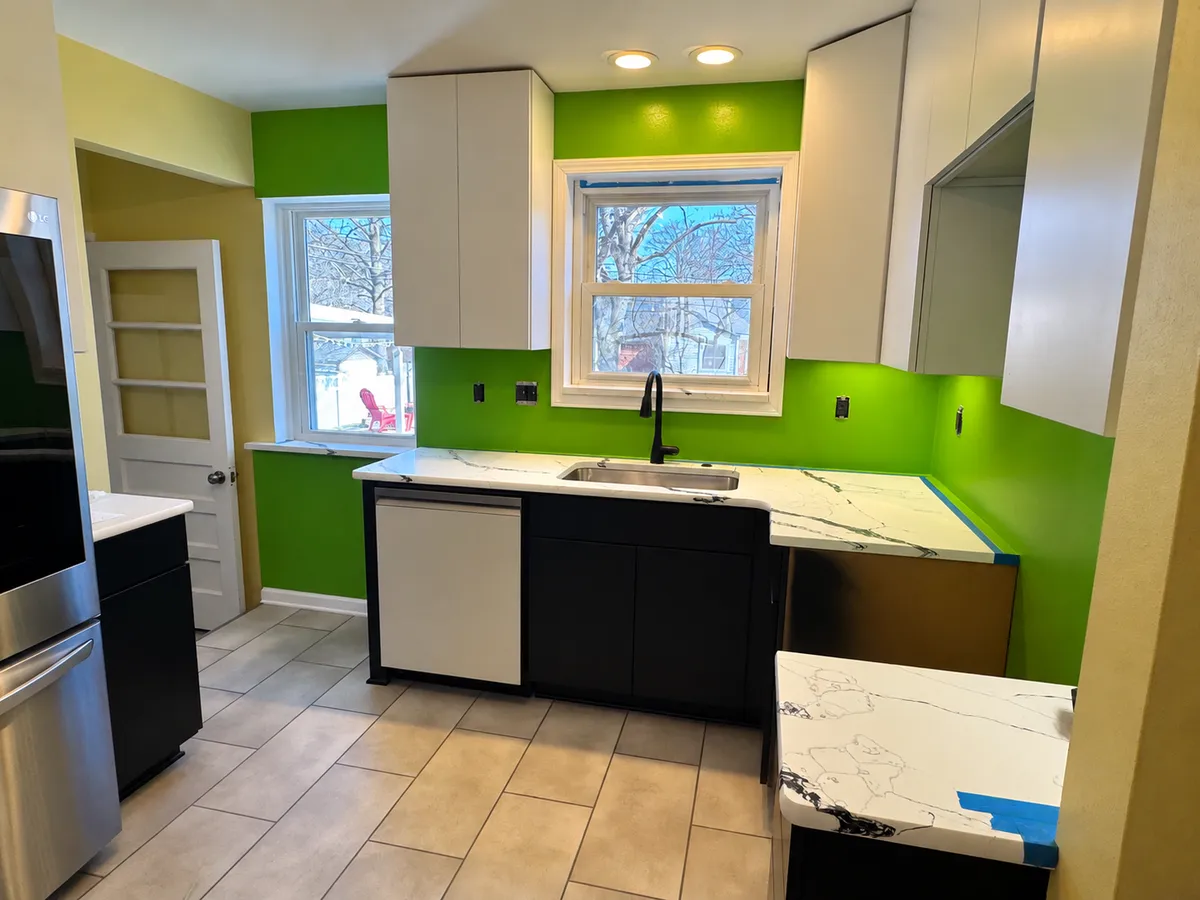 Residential kitchen with bright lime green painted walls, white upper cabinets, dark lower cabinets, and white countertops, showcasing custom interior painting.
