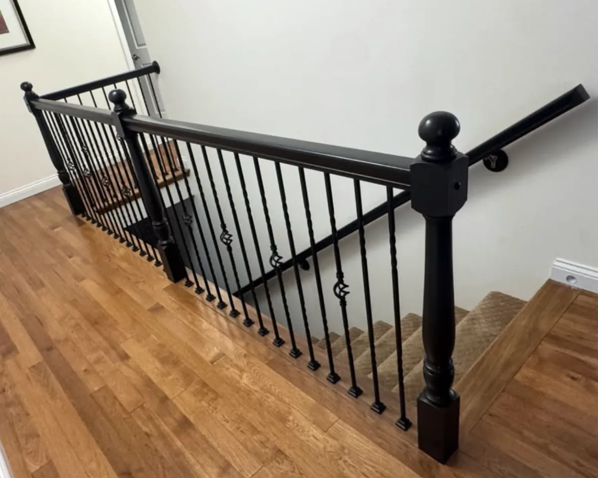 Black painted staircase railing, wood newel post, and handrail featuring detailed interior woodwork finishing in a residential home.
