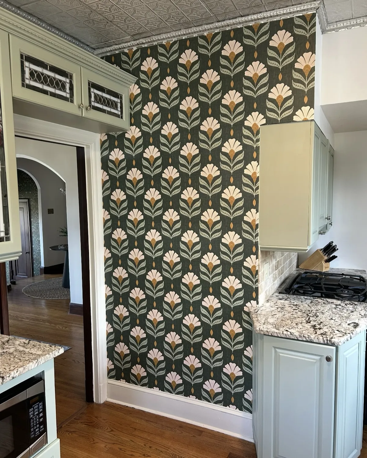 Decorative botanical wallpaper accent wall with green and cream floral patterns, coordinating cabinetry, and detailed interior trim.