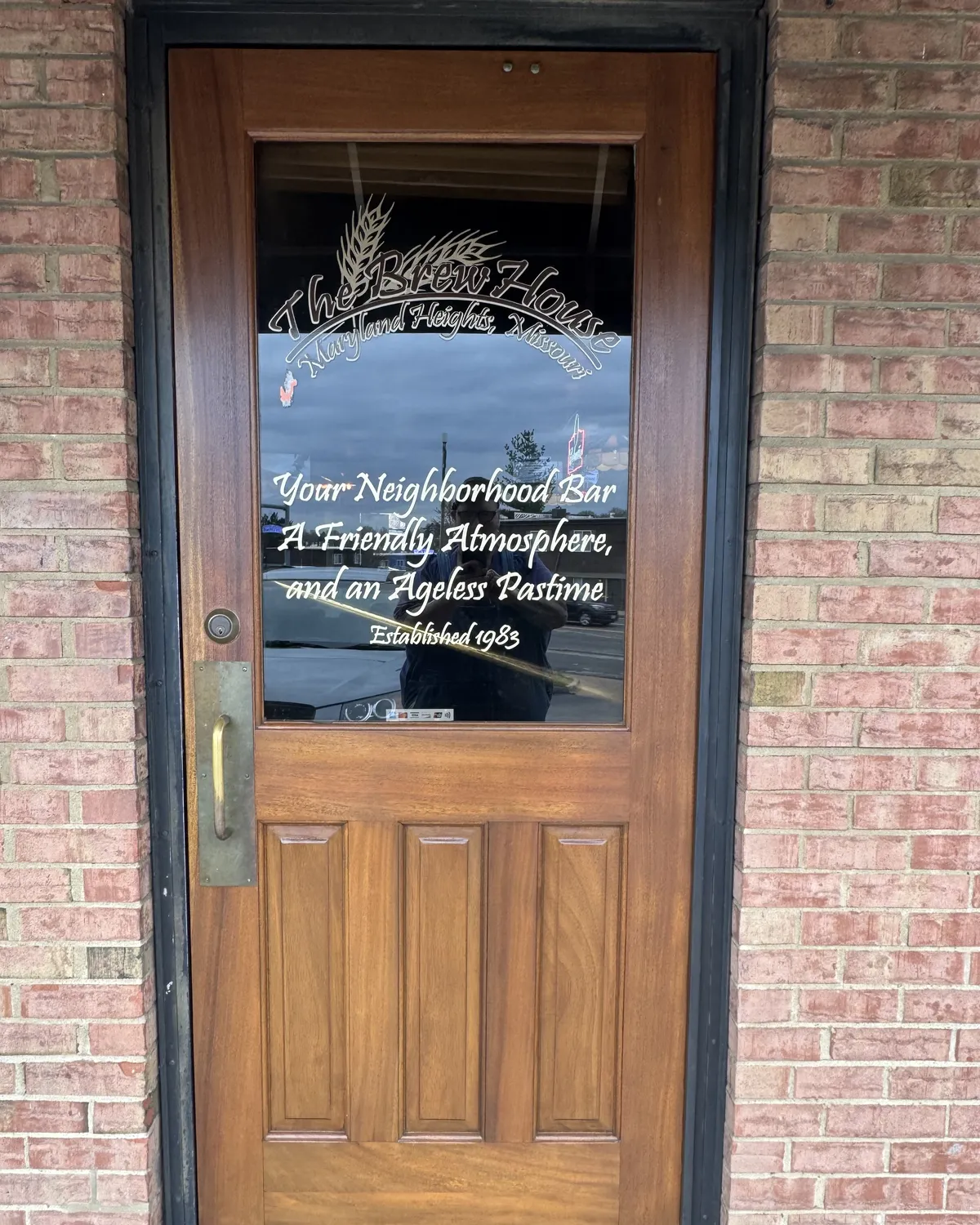 Wooden commercial entrance door with glass panel, natural wood grain, and stained finish set within a brick storefront in St. Louis.