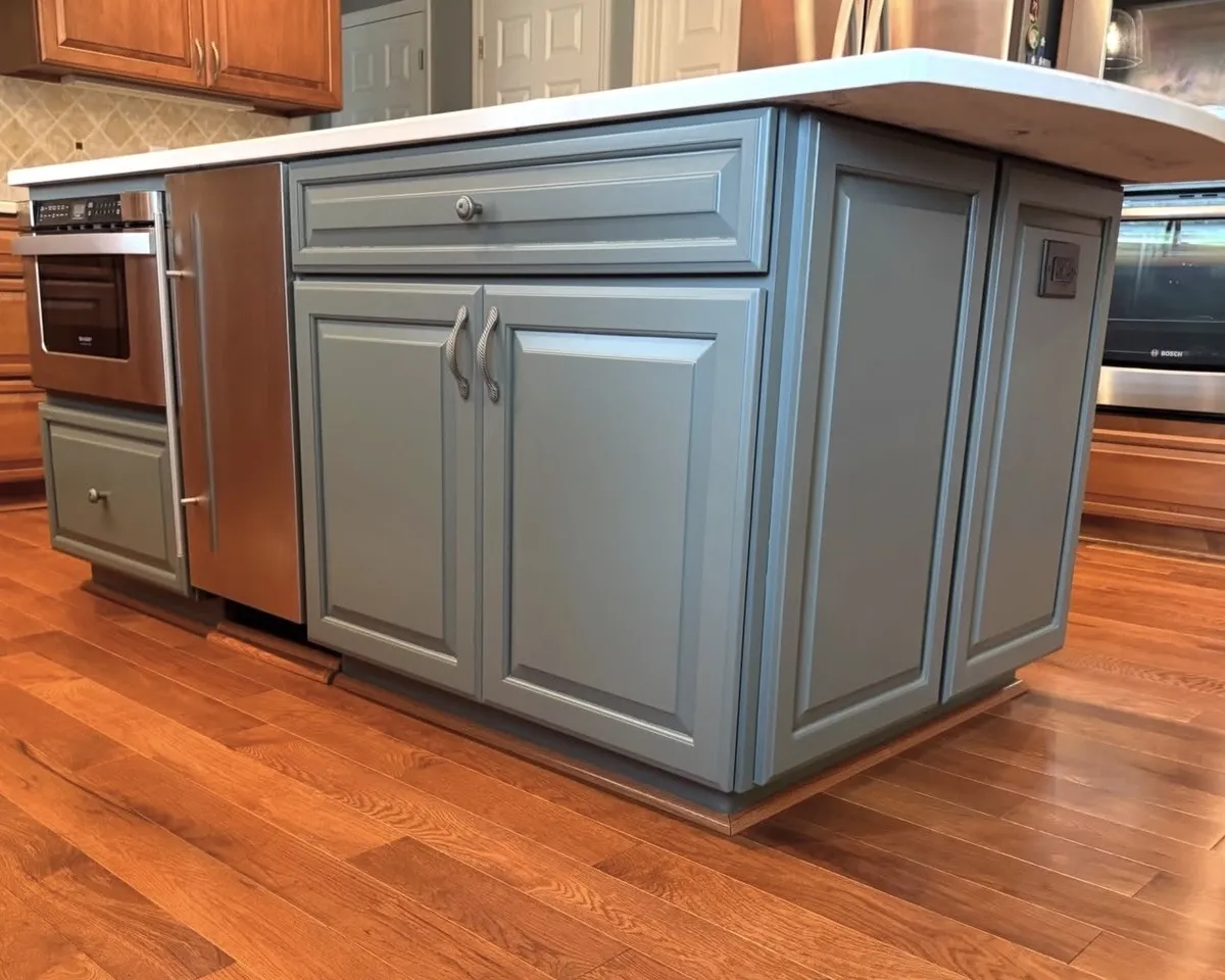 Kitchen island cabinet refinishing with blue-gray painted cabinet doors, drawers, and decorative molding beneath a white countertop.