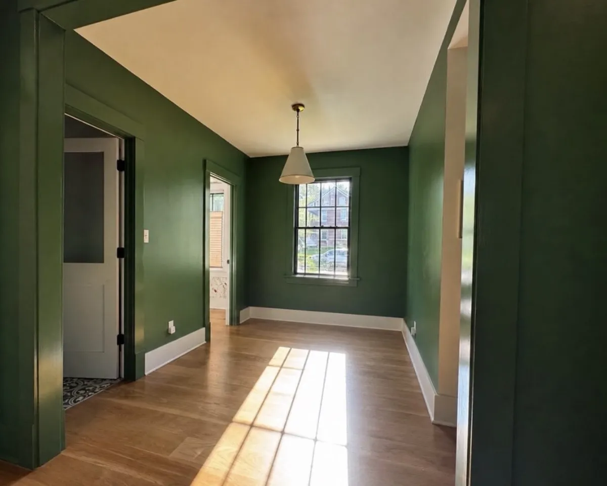Residential interior painting project featuring rich forest green walls, crisp white trim, natural hardwood floors, and a smooth wall finish.