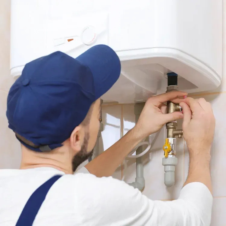 A plumber fixing a pipe connecting to a water heater.