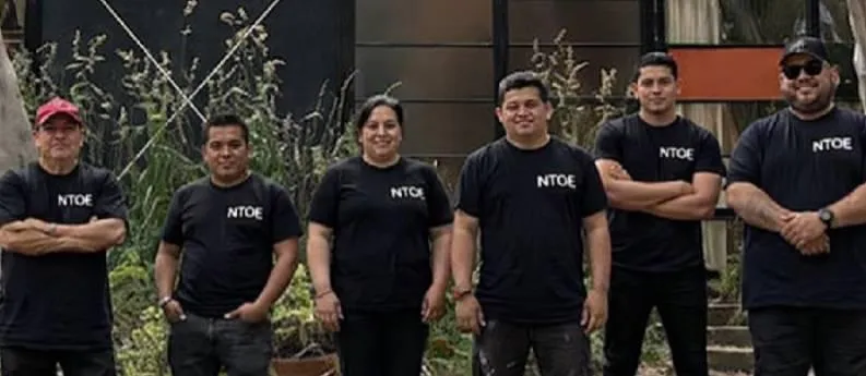 A smiling, multi-ethnic property management team stands together in front of a Santa Monica landmark, dressed in branded attire, exuding professionalism and approachability. The background is a sunny, palm-lined street.