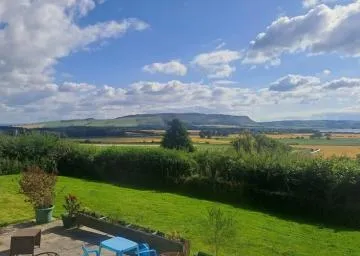 Scenic view of the countryside near Loch Leven, with green fields, golden farmland, and distant hills under a partly cloudy sky.