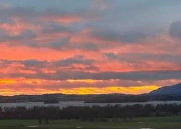 Scenic view of the sunset near Loch Leven, with green fields, golden farmland, and distant hills under a partly cloudy sky.