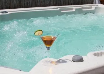Refreshing cocktail with a lime slice resting on the edge of a bubbling outdoor hot tub.